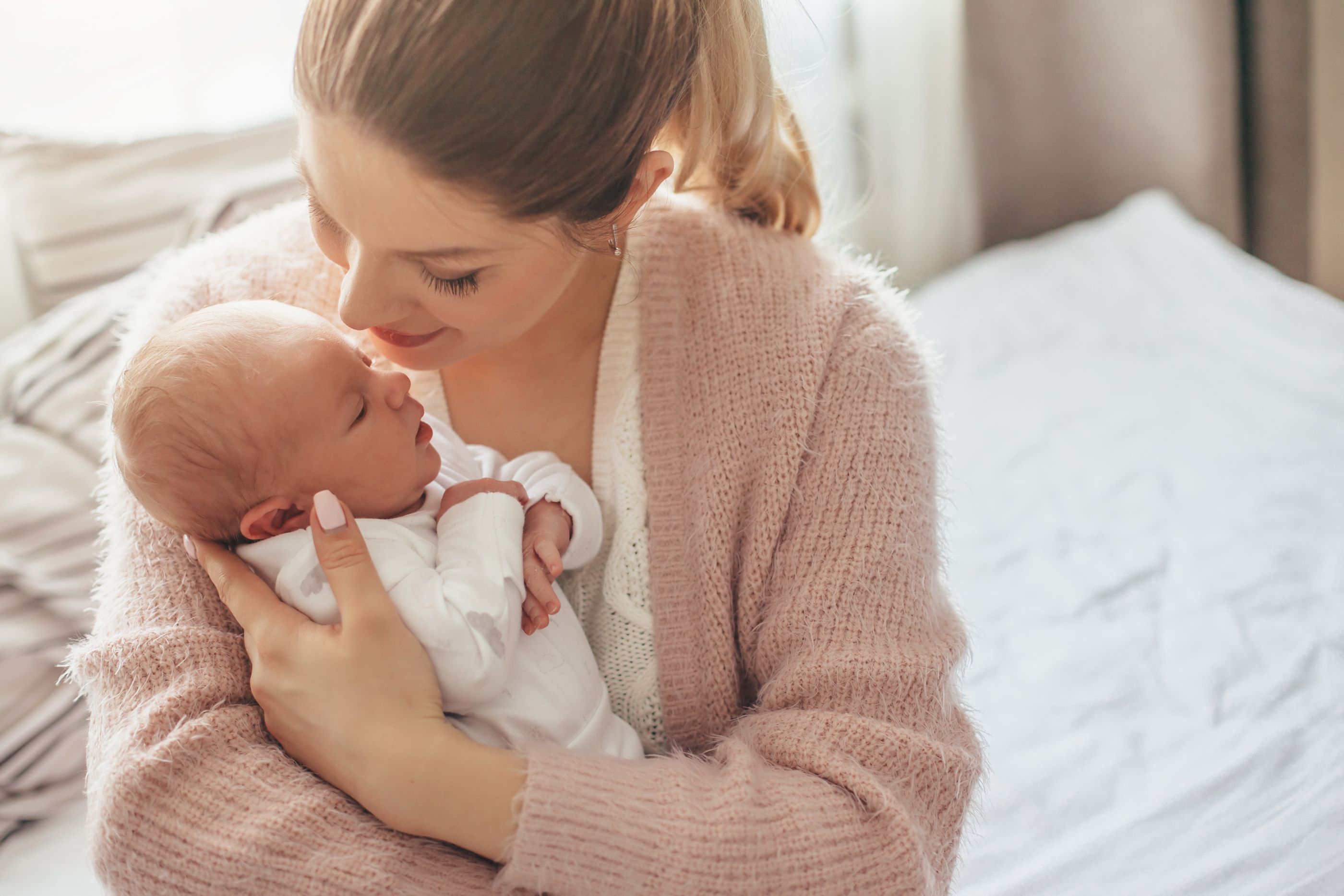 Home portrait of a newborn baby with mother on the bed. Mom hold